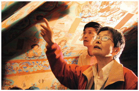 ▲樊錦詩（右一）在莫高窟第八十五窟壁畫修復(fù)現(xiàn)場。（敦煌研究院供圖）